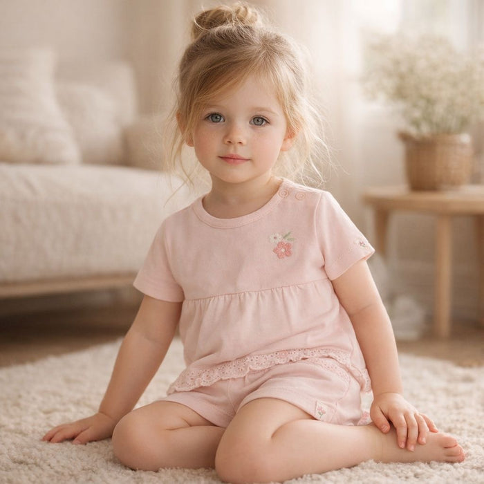 Baby Mädchen in rosafarbenem Set sitzt auf Teppich – hochwertige Kinderbekleidung in sanften Farben